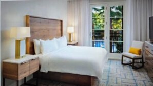 Habitación de hotel con una cama grande, dos mesitas de noche con lámparas, una silla y vistas al verdor por la ventana.
