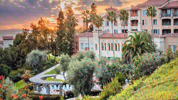 Un hotel con una entrada curva, palmeras y vista al océano al atardecer.
