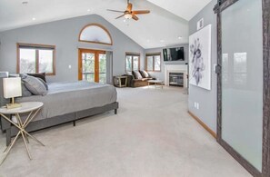 Relax in this serene bedroom with a large bed, ceiling fan, and mounted TV.