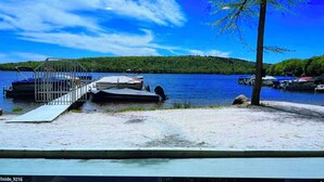 A lakeside dock with boats, a wooden pier, and a forested hill in the background.