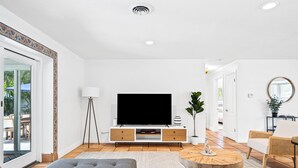 Un salon moderne avec un téléviseur à écran plat, un canapé gris, une table basse ronde et un fauteuil en osier.