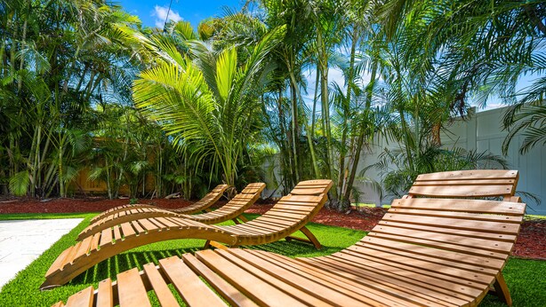 Des fauteuils de jardin en bois sont disposés en demi-cercle sur une pelouse bien entretenue, avec des palmiers en arrière-plan.