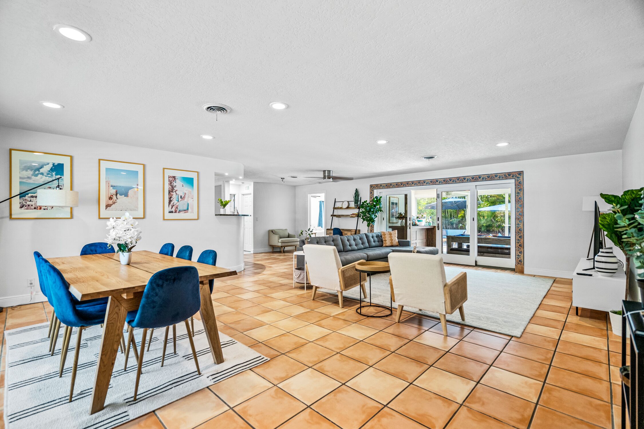 A spacious living area with a dining table, blue chairs, a sofa, and a large window offering a view of the outdoors.