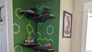 A corner wall with green hexagonal patterns, a wooden shelf unit with plants, a framed picture, and a dining table with chairs. - Cannabis Friendly House Minutes From Downtown Denver & Red Rocks (Denver)