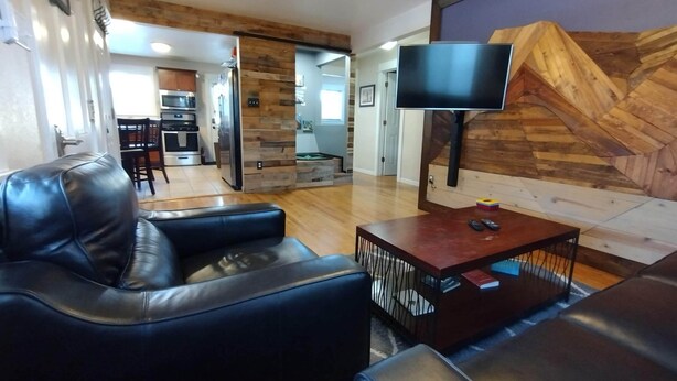 A modern living room with a leather sofa, a coffee table, and a flat-screen TV mounted on a wooden wall. - Cannabis Friendly House Minutes From Downtown Denver & Red Rocks (Denver)