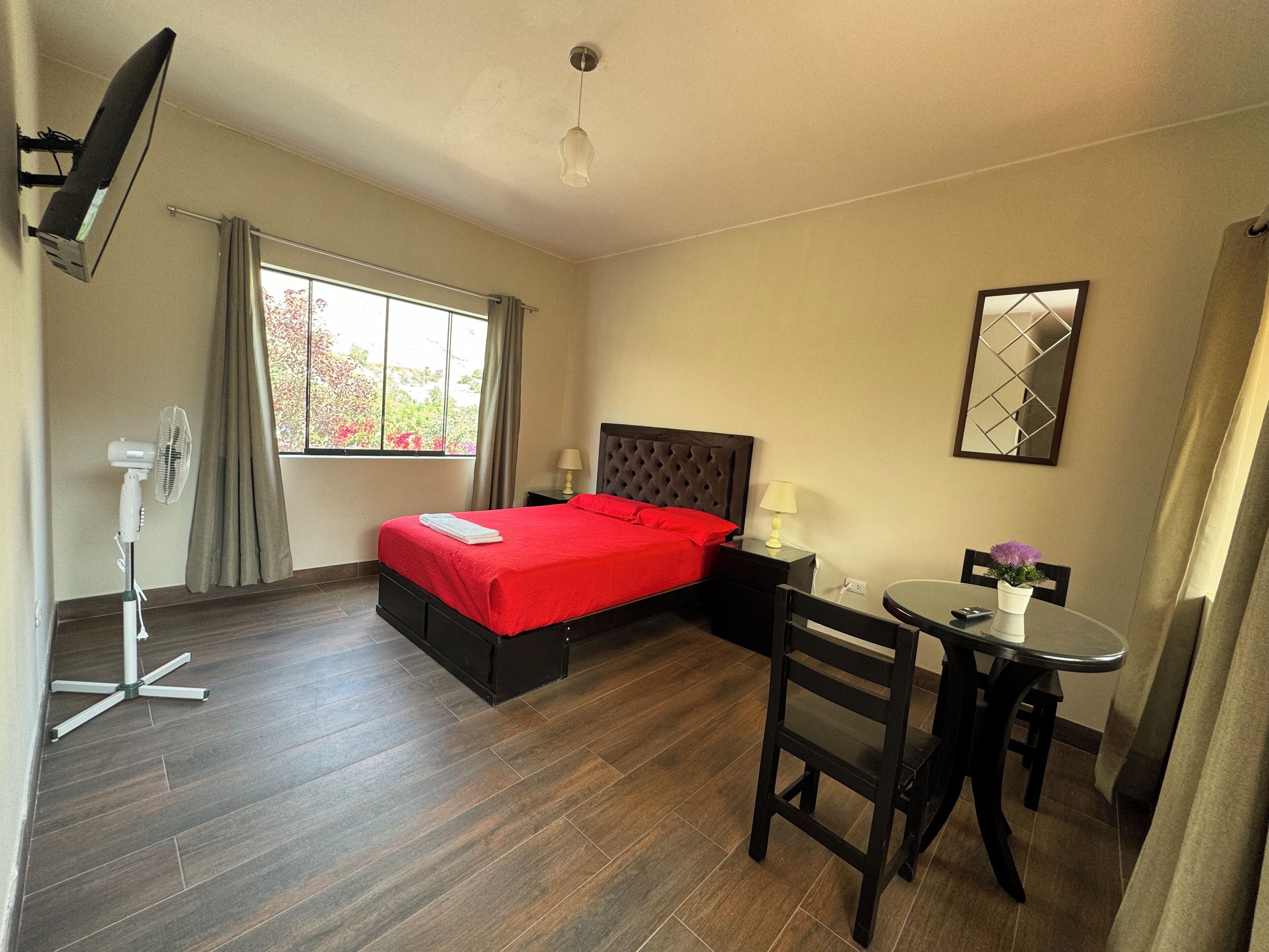 A hotel room with a bed, bedside table, lamp, chair, and a small table with a vase.