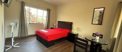 A hotel room with a bed, bedside table, lamp, chair, and a small table with a vase.