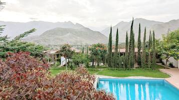 Una piscina rodeada de vegetación y montañas al fondo.