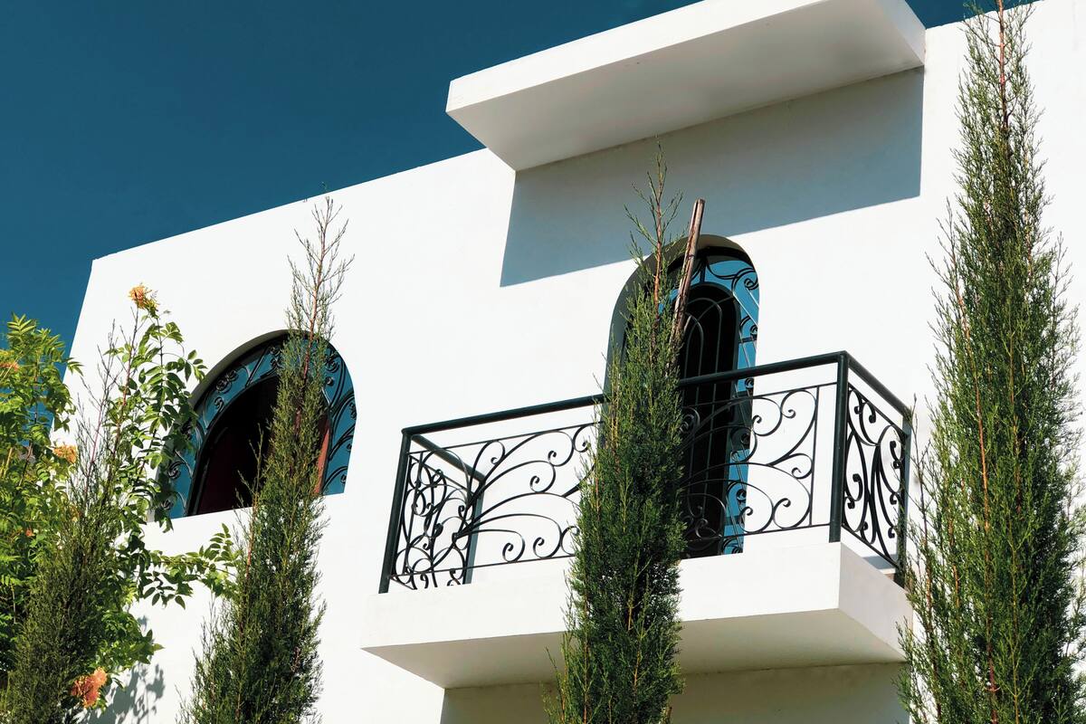 Un bâtiment blanc doté de deux balcons, chacun orné d’une balustrade en fer forgé et d’une fenêtre à cadre bleu.