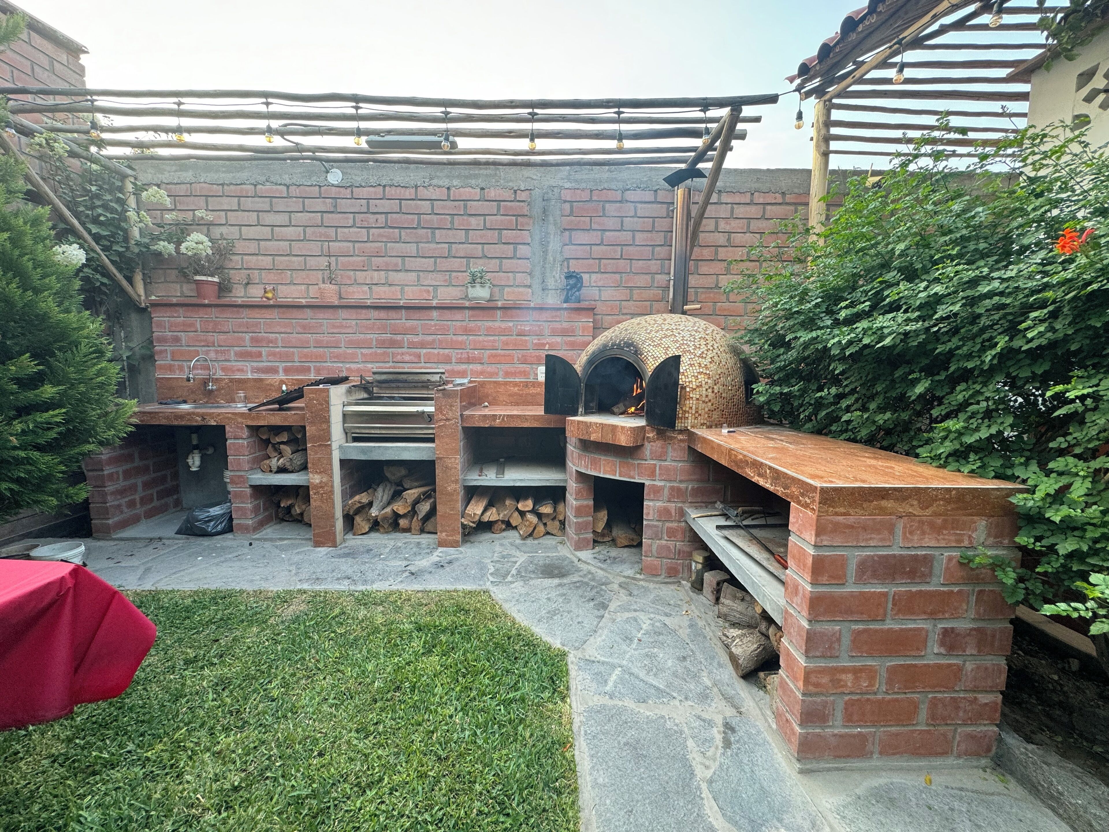 Cocina exterior de ladrillo con horno de pizza, parrilla y pileta.