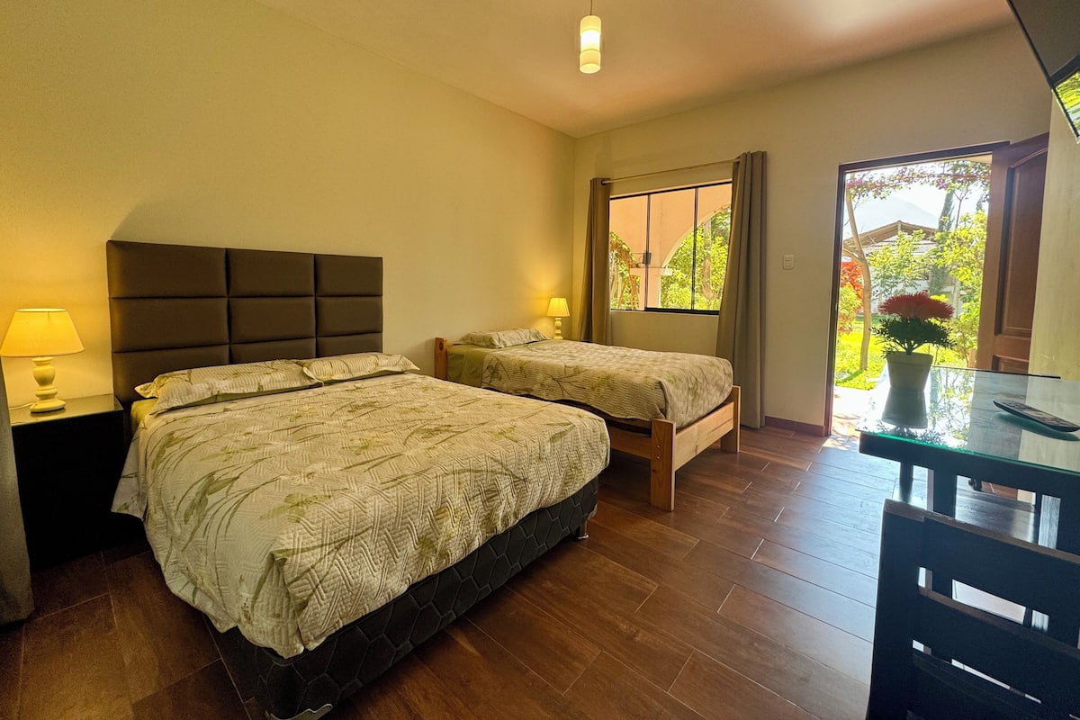 Une chambre d’hôtel avec deux lits, un bureau et une fenêtre donnant sur un espace verdoyant.