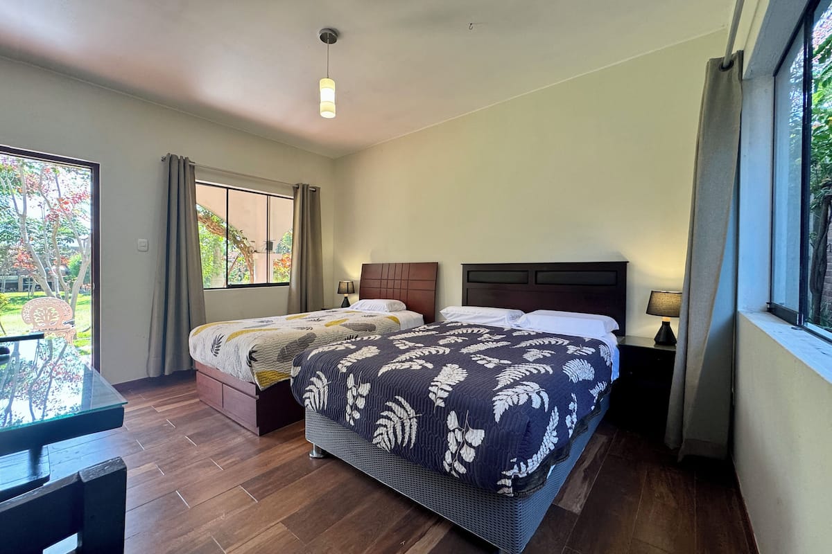 Une chambre avec deux lits, un plancher en bois, une fenêtre avec des rideaux et une table avec des chaises.