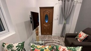 A compact living space with a dining area, a sofa, and a TV mounted on the wall. - 5 mins walk or rent a bike to ride to Turtle Beach. (Exuma)