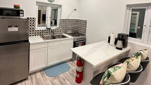 A modern kitchen with white cabinets, a stainless steel refrigerator, a gas stove, and a coffee maker. - 5 mins walk or rent a bike to ride to Turtle Beach. (Exuma)
