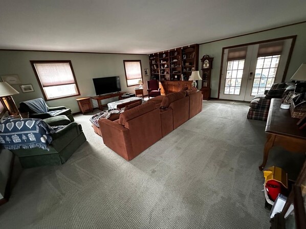 A living room with a large brown sofa, a television, a bookshelf, and a window with blinds. - Cozy beach cottage, steps from Lewes Beach (Lewes)