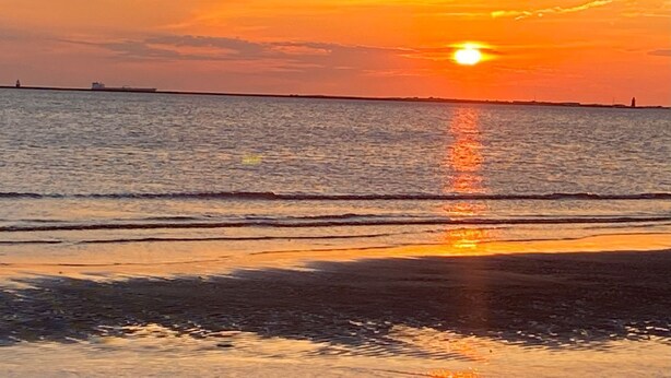 A sunset over a calm sea with a distant shoreline.