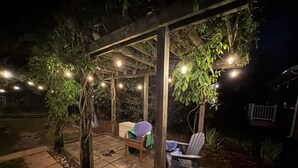 An outdoor patio with a pergola, string lights, a covered seating area, and a garden.