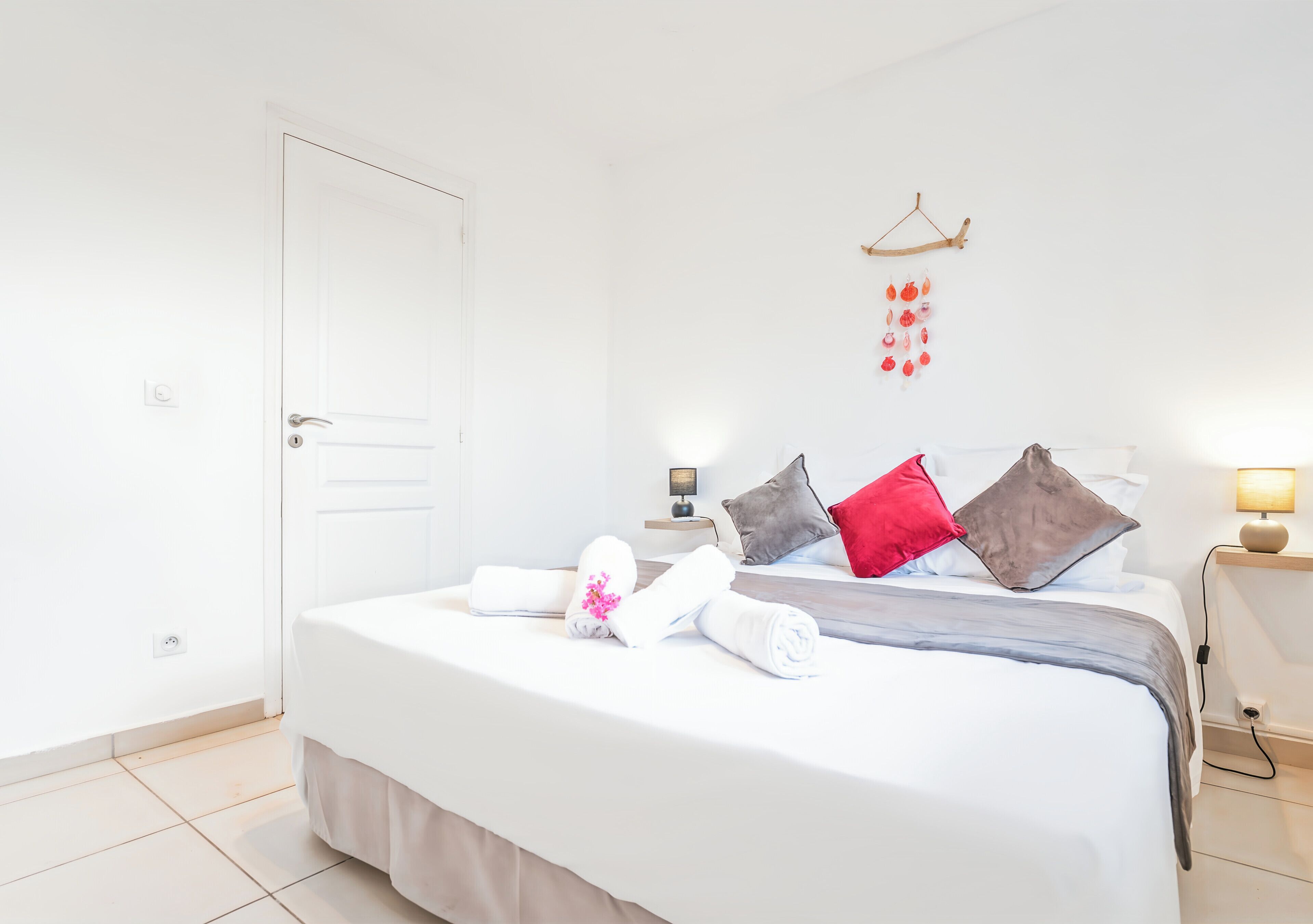 Un letto rifatto con cuscini e coperta, un comodino con una lampada e un elemento decorativo a parete.