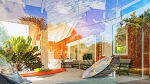 Moderni makuuhuone, jossa on sänky, pieni pöytä ja tuoleja. Ikkunan ulkopuolella on kasveja ja penkki.