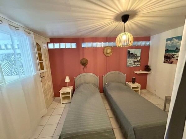 Une chambre avec deux lits, un ventilateur de plafond, une lampe fixée au mur et un tableau sur le thème de la plage.