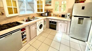 A compact kitchen with a gas stove, washing machine, oven, and a stainless steel refrigerator.