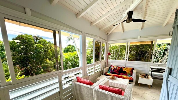 A sunlit room with large windows, a ceiling fan, and a wicker sofa with red cushions.