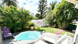 A wooden deck with a swimming pool, lounge chairs, and a garden with various plants.