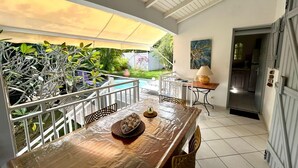 A covered patio with a wooden table, chairs, and a pool in the background.