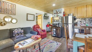 A cozy living room with a sofa, armchair, and coffee table, a kitchen with wooden cabinets and appliances, and a dining area with a table and chairs. - Ski-In Red River Retreat: Balcony, Mountain Views! (Red River)