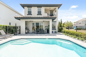 Une maison à deux étages avec une piscine, un patio doté de mobilier d’extérieur et un jardin clos.