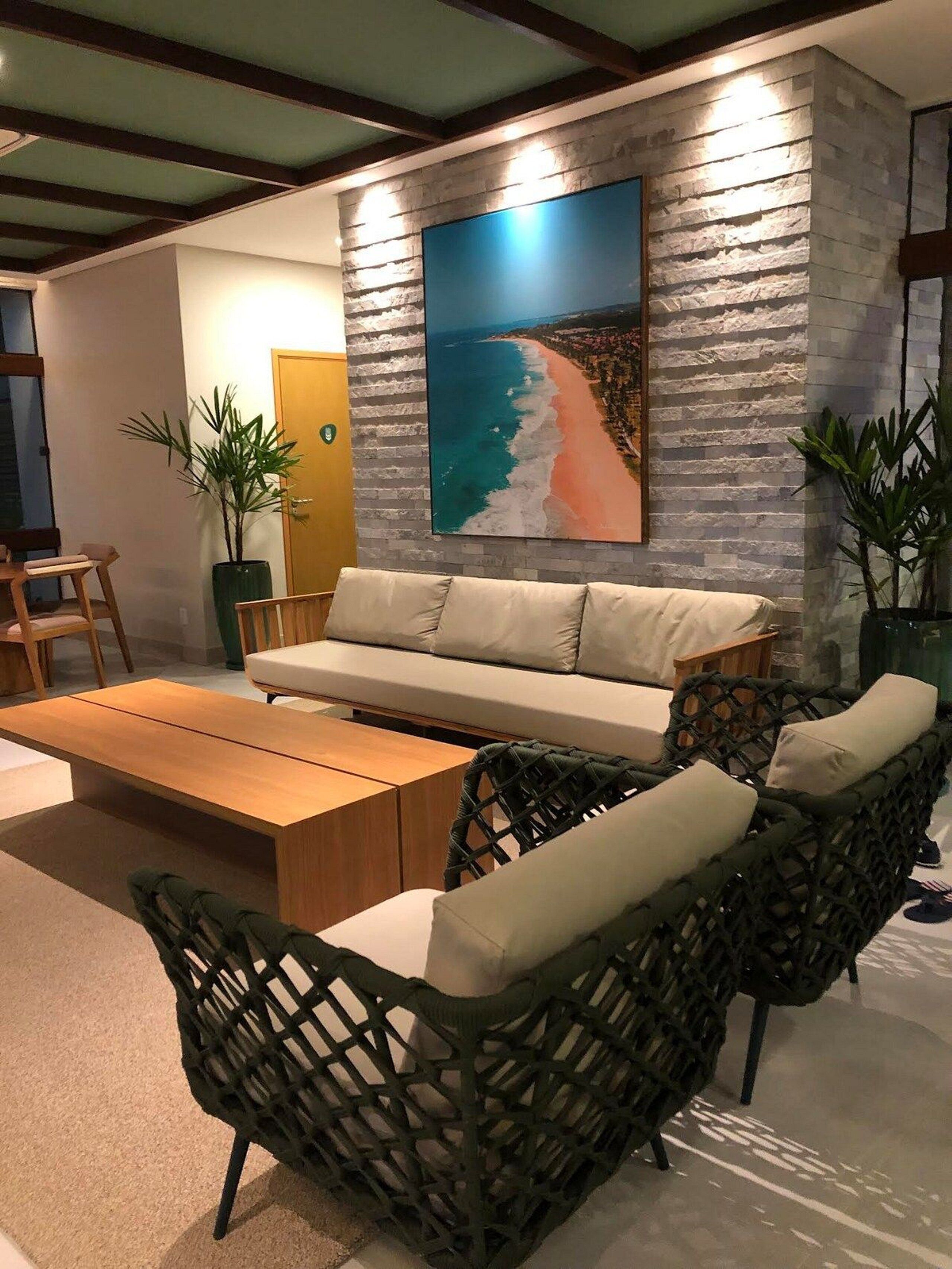 Ein modernes Wohnzimmer mit einer Couch, einem Couchtisch und Korbstühlen. An der Wand hängt ein großes Gemälde vom Strand.