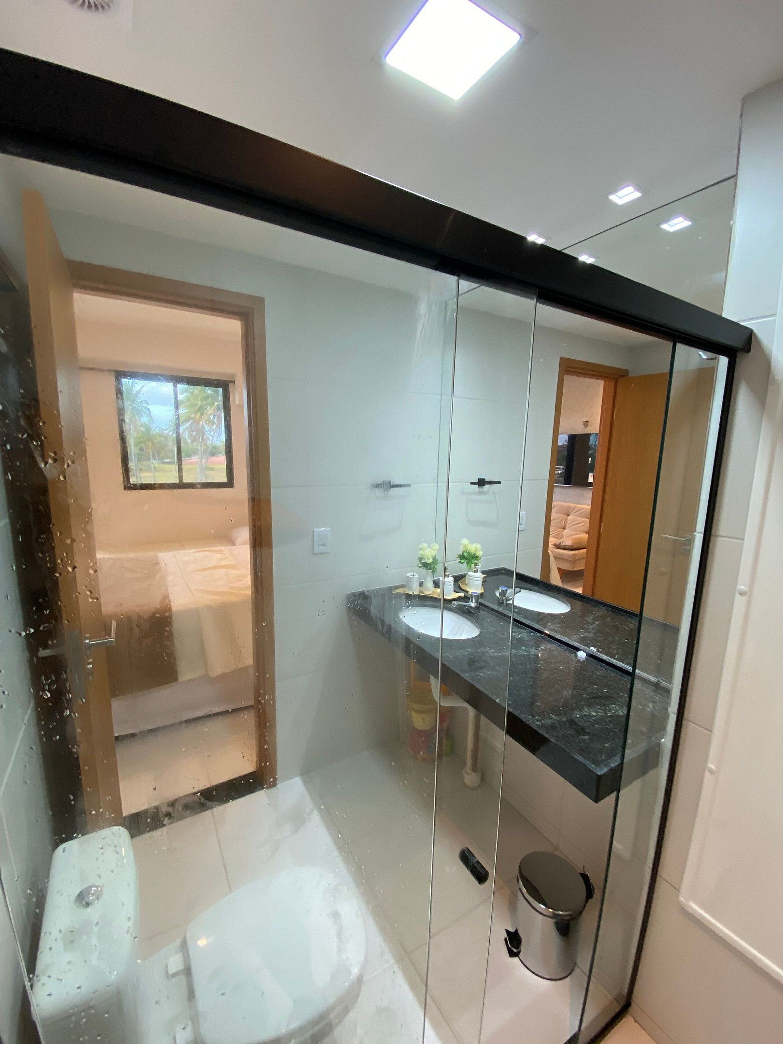 Un baño moderno con mampara de vidrio, dos lavamanos, un inodoro y zona de ducha.