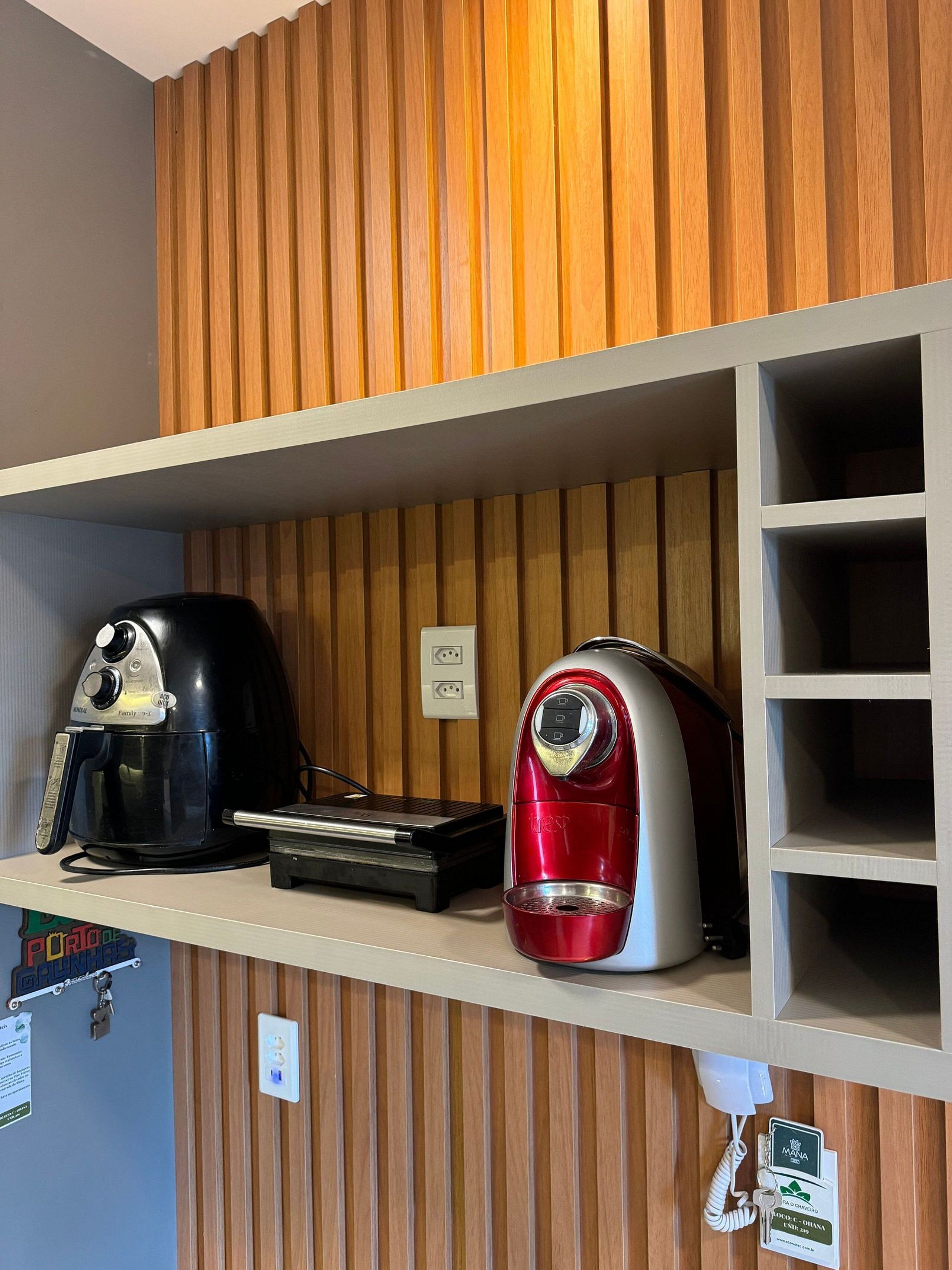 A kitchen area with two coffee makers on a shelf, a phone, and a wall-mounted light switch.