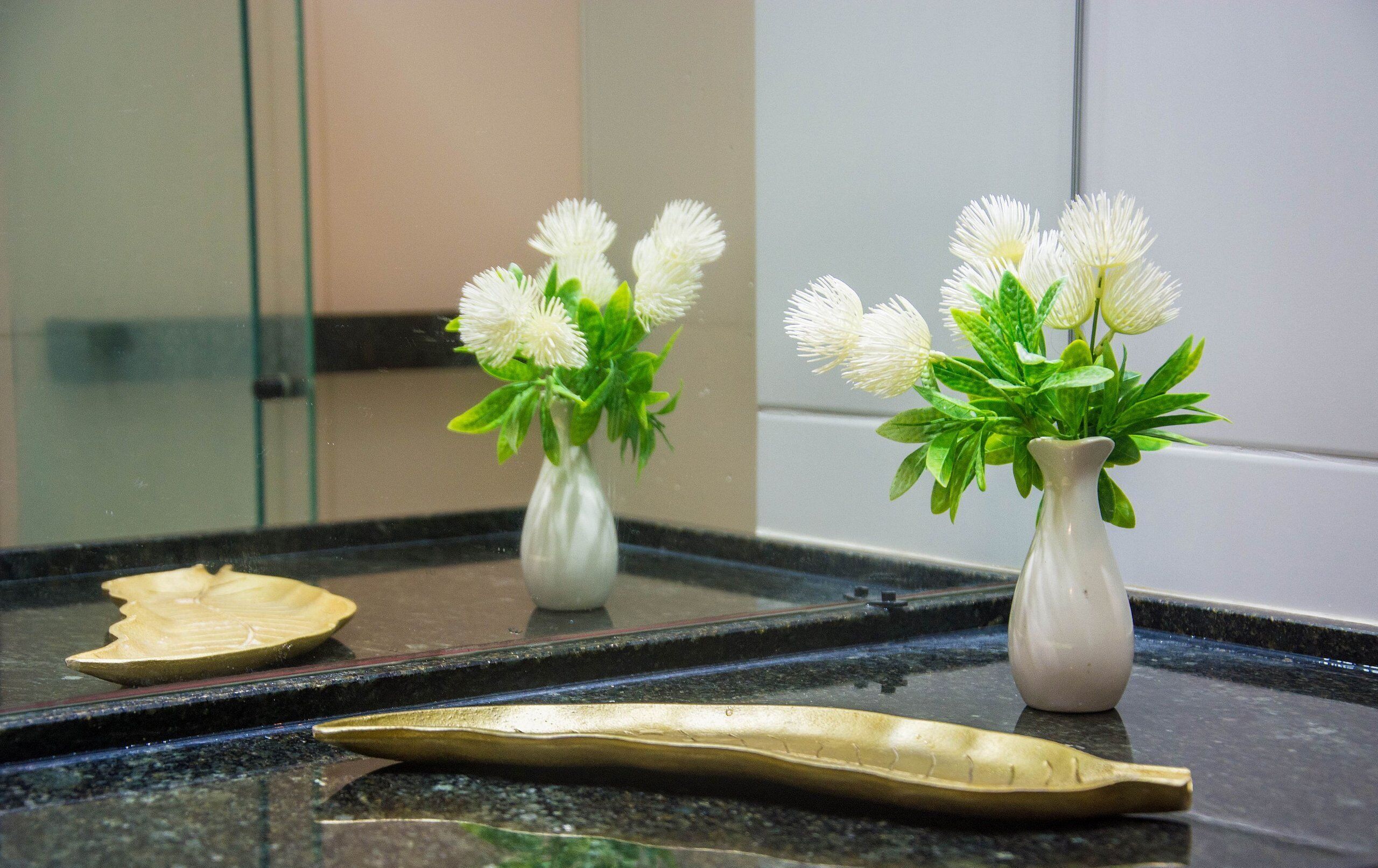 Deux vases blancs ornés de fleurs blanches, posés sur un comptoir réfléchissant.