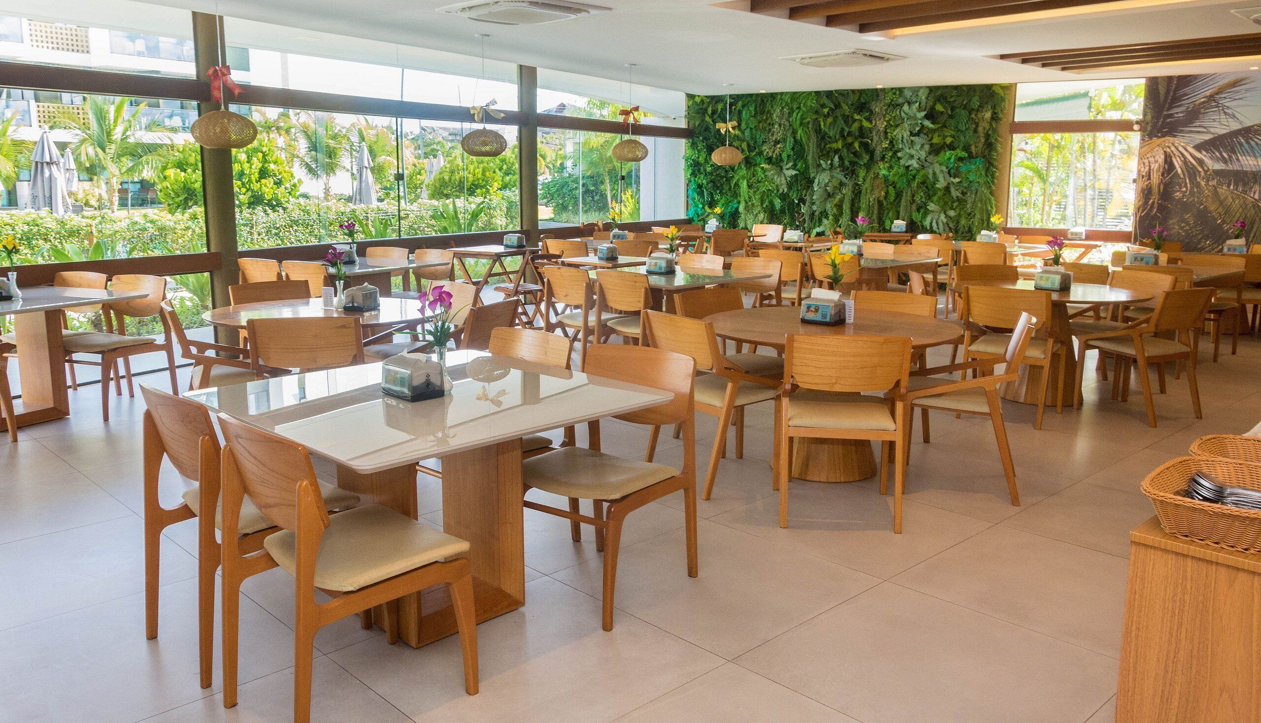 Un restaurant spacieux avec des tables et des chaises en bois, de grandes fenêtres donnant sur un paysage verdoyant.
