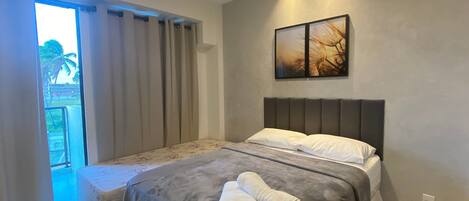 Un dormitorio con cama, cortinas, un cuadro y vistas al exterior.