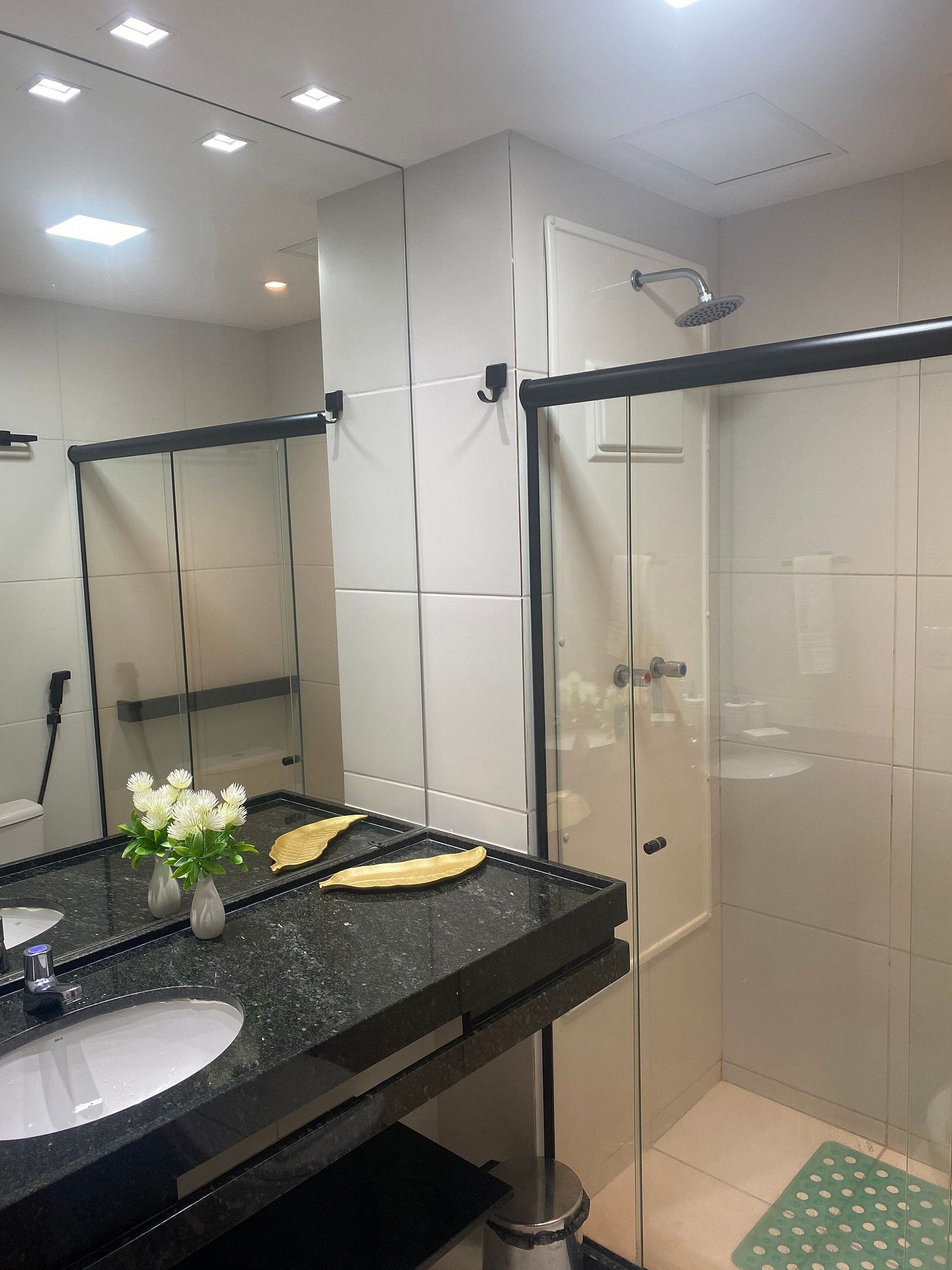 A modern bathroom with a black countertop, a large mirror, and a glass shower enclosure.
