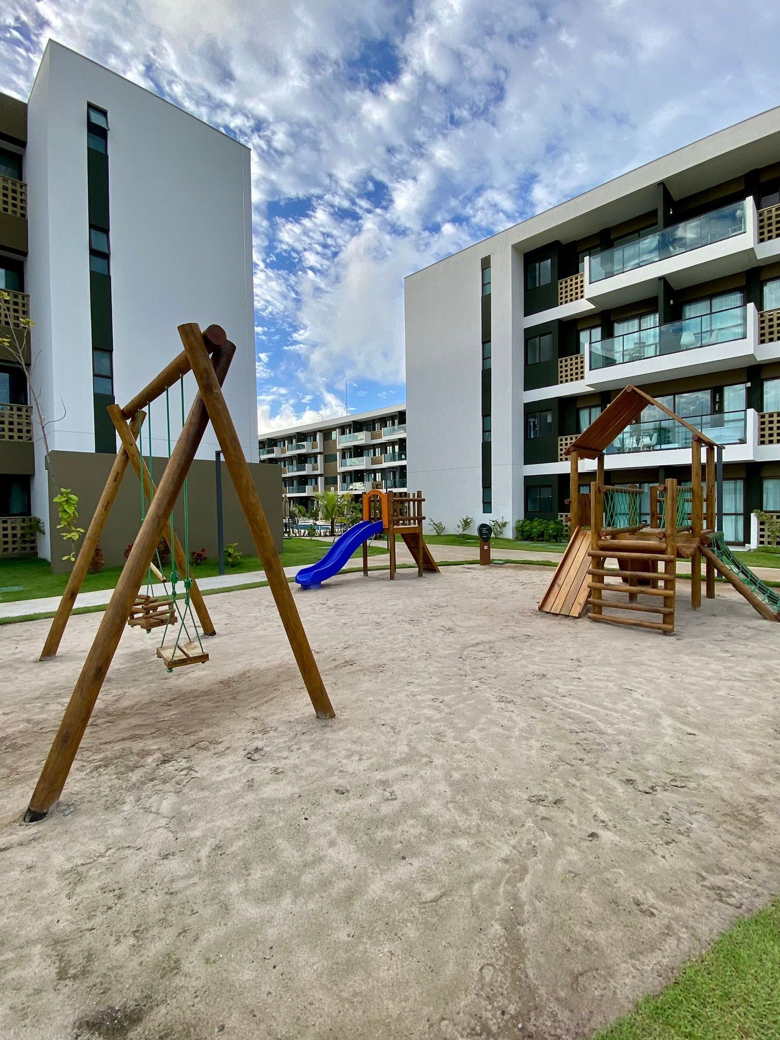 A playground with swings and slides, surrounded by a building with multiple balconies and windows.