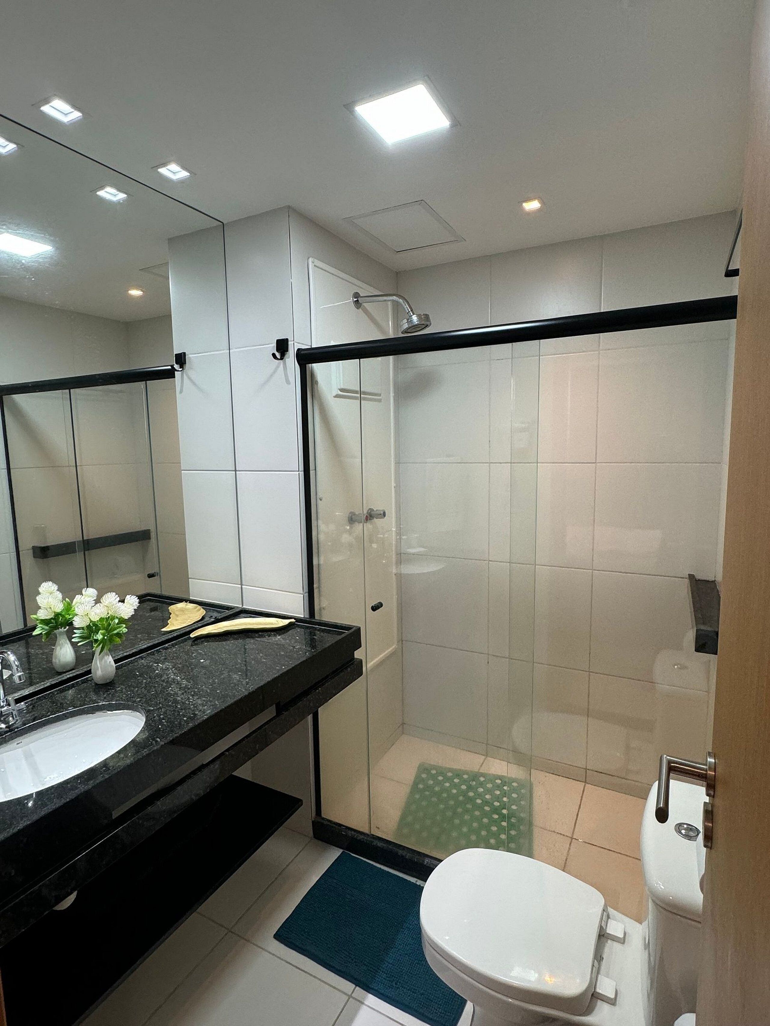 Une salle de bain moderne avec un plan de toilette noir, un lavabo blanc et une cabine de douche en verre.