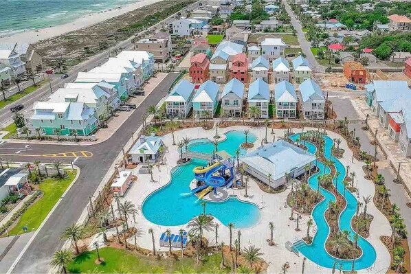 A resort with a central pool area, multiple buildings with varied roof colors, and a beach in the background. - 5 O Clock Somewhere (Panama City Beach)
