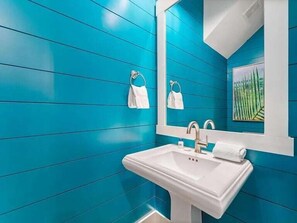 A bathroom with a white sink, a large mirror, and teal walls. - 5 O Clock Somewhere (Panama City Beach)