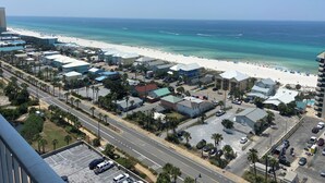 Un hôtel situé sur la côte, avec vue sur la plage, un parking et une route bordée de palmiers.