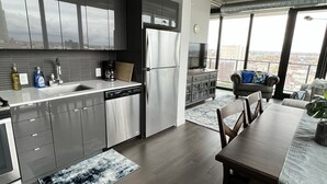 Une cuisine moderne avec des meubles de couleur sombre, des appareils en acier inoxydable et une grande fenêtre donnant sur un paysage urbain.