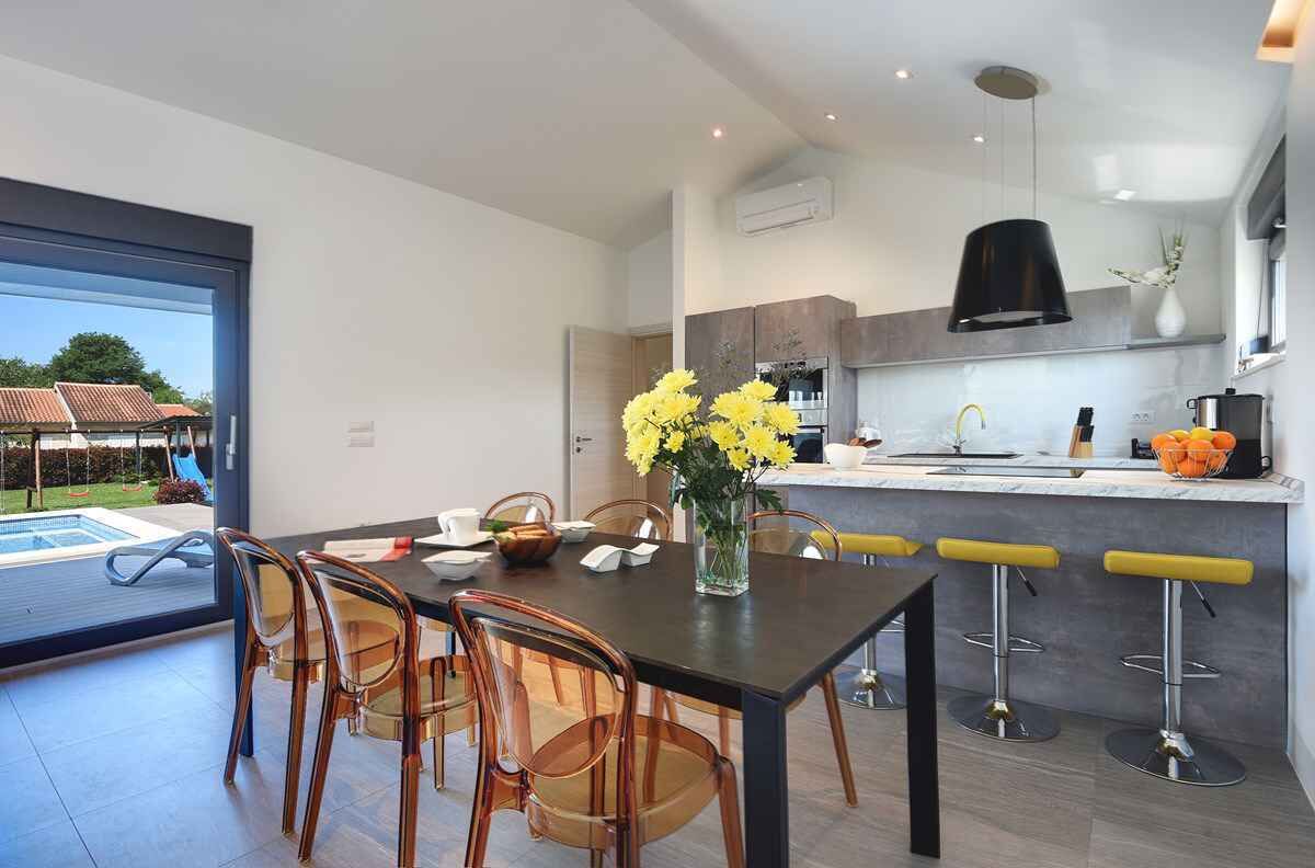 A modern kitchen with a dining area, a large window, and a view of a pool.