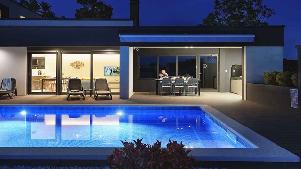 A modern house with a swimming pool, outdoor dining area, and a well-lit interior. - Villa with swimming pool and playground (Valbandon)