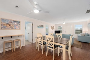 A dining area with a wooden table and chairs, a ceiling fan, and a kitchen in the background.