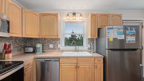 Una cocina con armarios de madera, un refrigerador de acero inoxidable, un lavavajillas y una ventana con persianas.