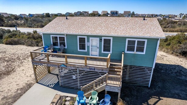 Una casa de playa de dos pisos con un balcón, mobiliario exterior y una terraza.