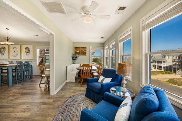 A spacious living room with a large window, a ceiling fan, and a dining area with a view.