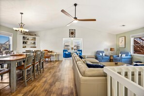 A spacious living area with a dining table, chairs, a sofa, and a ceiling fan.